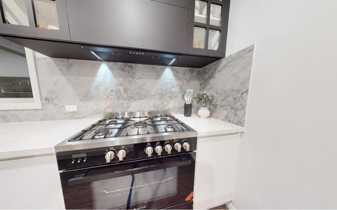 Modern kitchen features a stainless steel gas stove with marble backsplash, white countertops, and black cabinetry above